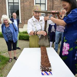 Burgemeester Avine Fokkens en wethouder Ojanne Changs snijden de speciale turfcake aan met een originele turfsteker